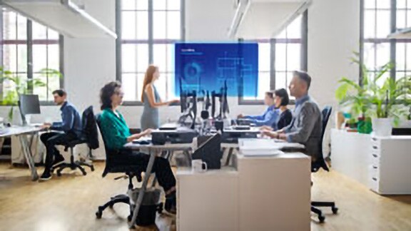 Employees sitting at a table watching a presentation with the OpenBlue Enterprise Manager ​overlaid on the screen