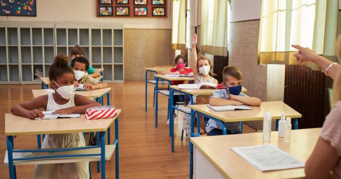 Elementary students in a classroom, with one student with their hand raised