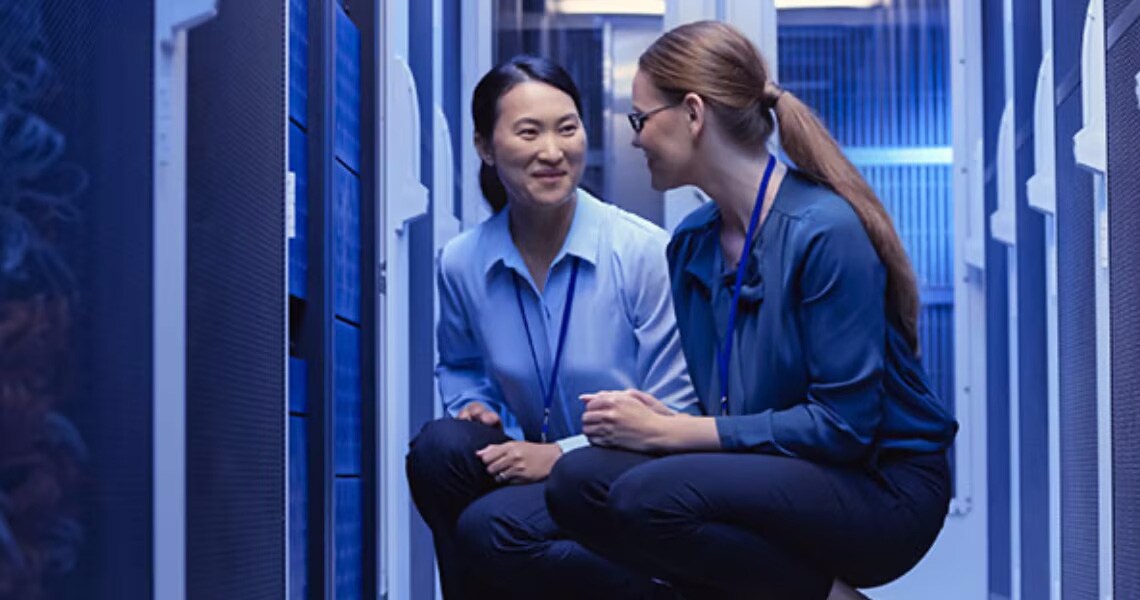 Two female engineers kneeling down and having a conversation in a data center