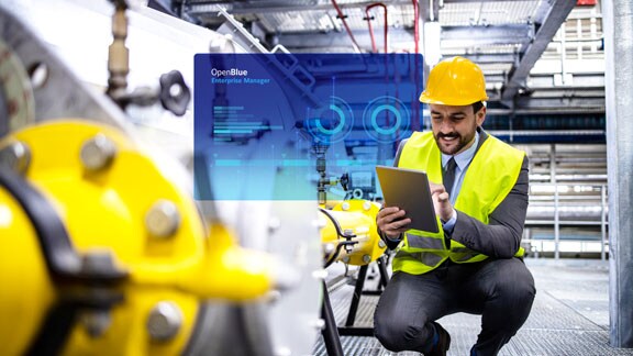 A maintenance engineer looking at a tablet in a factory, with a blue OpenBlue poster overlaid in the foreground