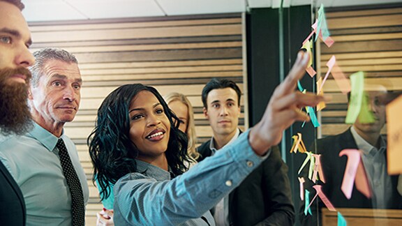 A woman pointing at sticky notes on a glass panel to her colleagues