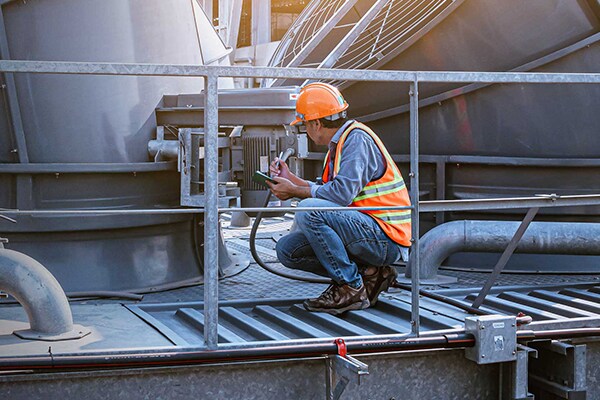 A mechanic crouching and examining a device in an HVAC plant