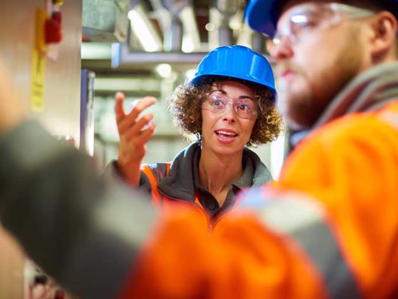 Close-up of a male mechanic fixing a device, while a female mechanic explains something in the background