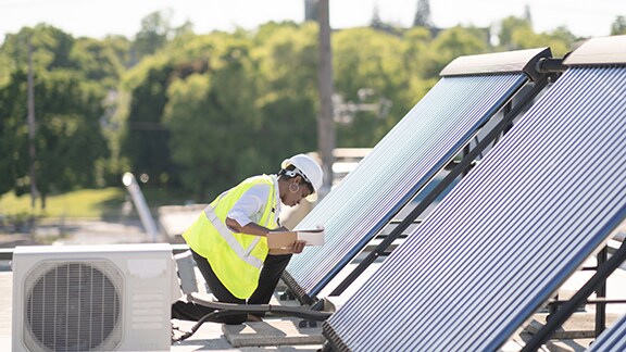 A female engineer writing on a clipboard near a set of solar panels